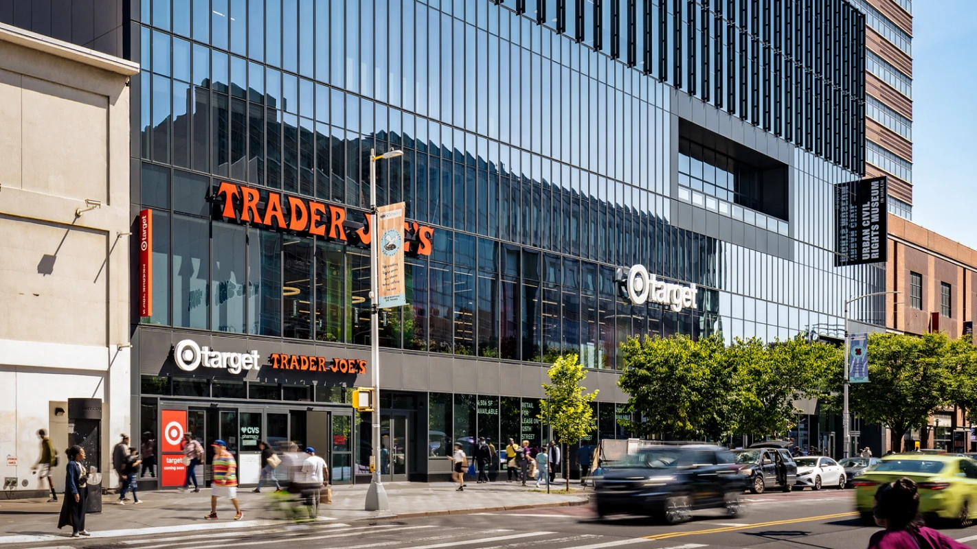Busy city sidewalk outside Target and Trader Joe’s under sleek glass-fronted retail architecture