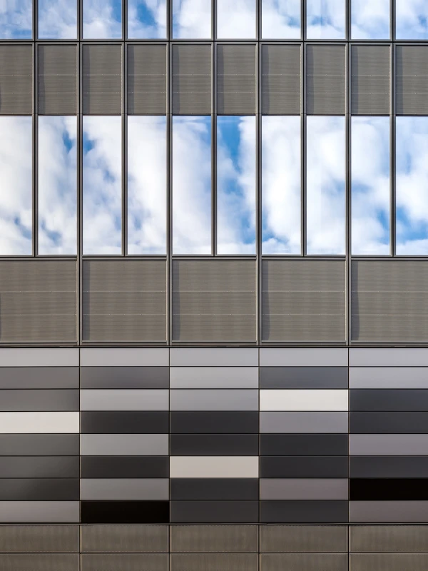 Reflective vertical windows with blue sky and clouds above a modern gradient panel façade